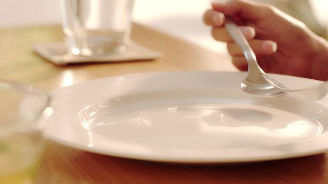 Female hands holding a fork and spoon next to an empty plate 