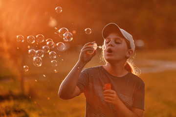 A child of 10-12 years old blows soap bubbles in the park at sunset. A school-age girl...