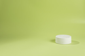 An empty stage with one white podium a top hat on a green background and a shadow from sunlight