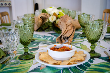 Mesa decorada estilo tropical con aperitivos, vajilla verde cristal y flores