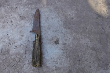 An old rusty knife with a rotten wooden handle found in the ground. I'm lying on the gray concrete floor.
