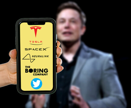 MADURAI, INDIA 2022 MAY 23 : Elon musk's own companies logos on holding smartphone and blured Elon Musk in the background.