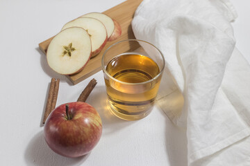 A glass with apple cider or juice on a light background, apples, a white cloth nearby
