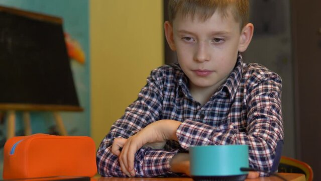 caucasian boy 8-9 years old sitting at home at the table talking with a smart speaker receives information from gadgets assistants. school age boy uses smart speaker