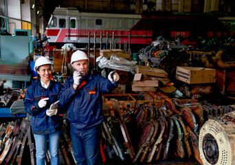Caucasian factory worker or technician use walkie talkie and stand beside Asian factory woman in front of the train and spare part of machine in workplace area.