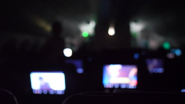 Dark passenger cabin of airliner, blurry view, people sleep and watch movies during long-haul flight. Footage includes original sound, hum of plane engine and the noise of people
