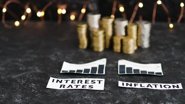 interest rates and inflation texts and graphs showing rates going up and consumer spending going down in front of stacks of coins