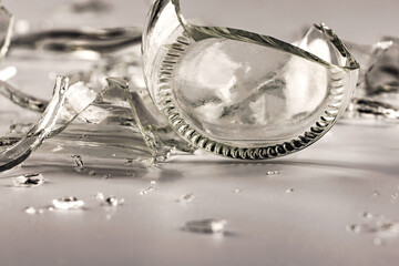A glass bottle broken into many fragments on a gray background.