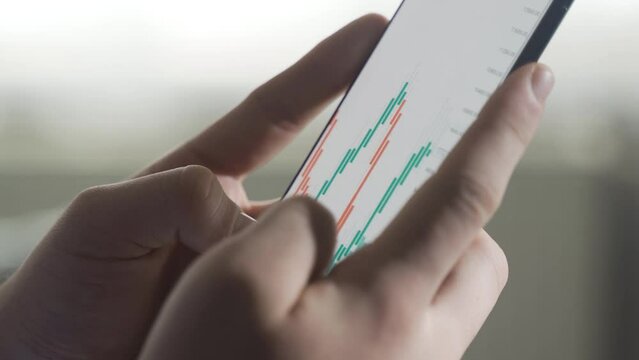 Looking at the stock market, stocks, investment charts on the phone, close-up.
The man who looks at the stock market, stocks, investment charts on the phone is happy and wins.
