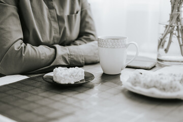 middle-aged woman sitting at the table in the cosy kitchen in the apartment and drinking tea with apple pie, cozy autumn days, black and white atmospheric photo