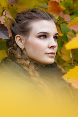 A beautiful serious girl stands near a tree with yellow foliage.