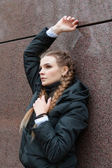 Beautiful serious girl stands against the wall.
