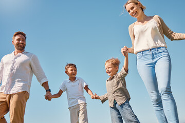 Family, children and sky with a mother, father and boy siblings walking hand in hand outdoor in summer. Freedom, love and kids with a brother holding hands with his parents while on a walk together