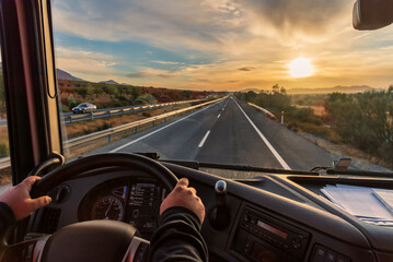 View from the driver's seat of a truck of the highway and a landscape of fields at dawn, with a dramatic sky. - obrazy, fototapety, plakaty