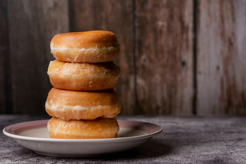 Glazed donuts, placed one on top of the other on a plate, with a rustic wooden background.