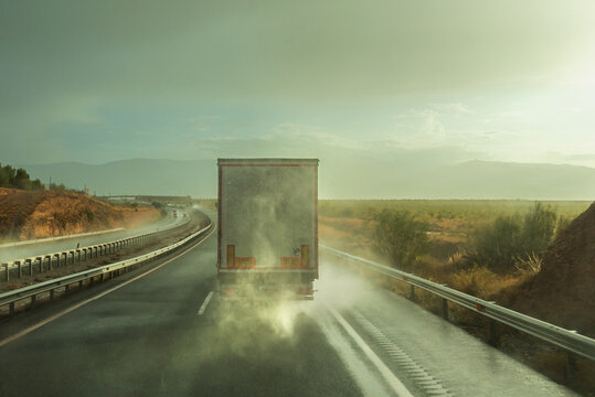 Truck driving along the highway on a very rainy day raising a cloud of water in its path, rear view.