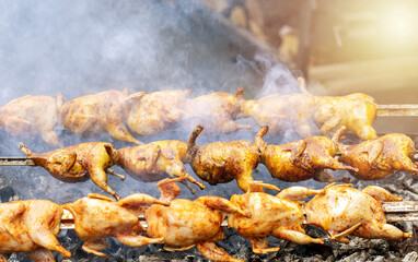 street food national holiday city day.barbeque meat with vegetables,quail birds on grill, corn cob,potatoes and grilled minced meat rolls.man hands in gloves turn food,smoke from coal fire