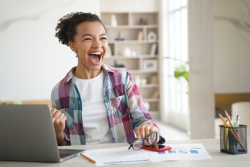 Excited happy mixed race high school girl student celebrating personal achievement sitting at laptop