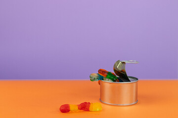 Gummy worms crawling out of a tin can, one escapes