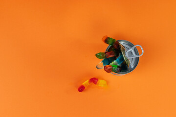 Gummy worms crawling out of a tin can, one escapes