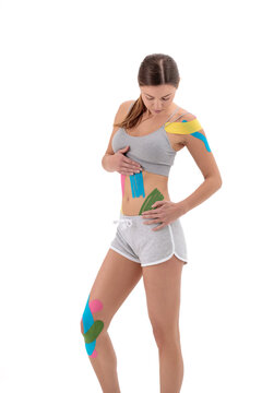 Sportswoman with kinesio tape on the shoulder, knee, stomac joint stands on a white background.