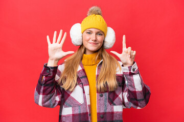 Young beautiful woman wearing winter muffs isolated on red background counting seven with fingers