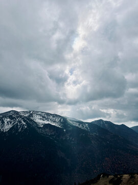 prześwitujące przez chmury światło słoneczne nad ośnieżonymi szczytami gór © Maciej