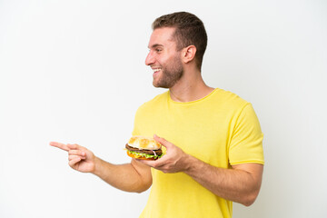 Young caucasian man holding a burger isolated on white background pointing to the side to present a product