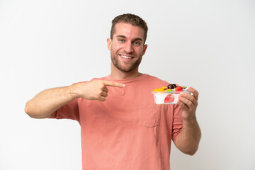 Young caucasian man holding a bowl of fruit isolated on white background and pointing it
