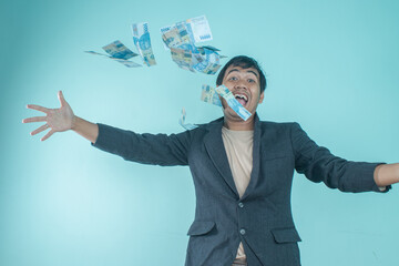 A successful Asian businessman wearing a black suit is throwing money away so the money is flying on a blue background