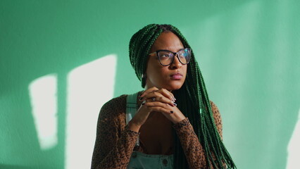 One contemplative black adult girl with subculture box braids staring out home window in mental reflection. Pensive african American young woman