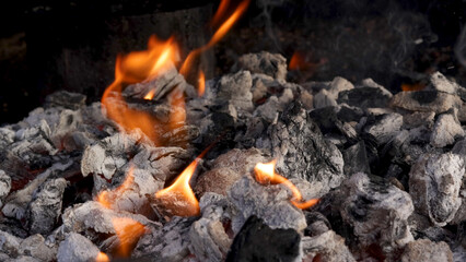 Small flames of fire coming out of hot barbecue ash and charcoal