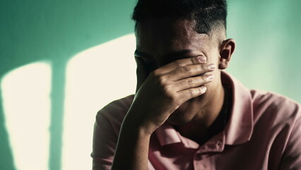 Depressed young man covering face with hand feeling ANXIETY. Suffering person with negative emotions remembering TRAUMA