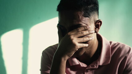 Depressed young man covering face with hand feeling ANXIETY. Suffering person with negative emotions remembering TRAUMA