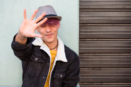 Young male boy smile and put his hand against to stop and protect or protest. Wall in background copy space. Concept of youth guy people in stop gesture. Colorful image of teenager portrait