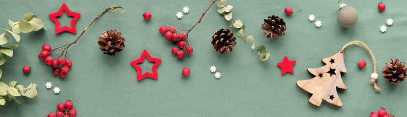 WInter panoramic banner with natural Xmas decor. Christmas or seasonal background in green and red. Flat lay, panorama with hawthorn berry, eucalyptus, trinkets, balls, stars, cones, sugar snowflakes.