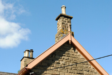 Chimneys and Wooden Barge Boards on Gable of Old Stone Building seen against Blue Sky