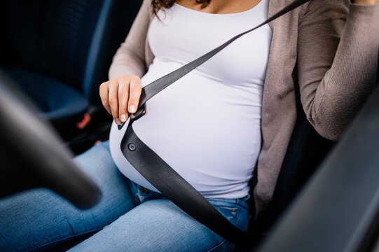 Closeup of pregnant woman sitting in car and fasten seat belt