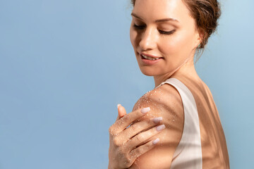 A beautiful attractive woman applies a cosmetic natural scrub to her shoulder and smiles