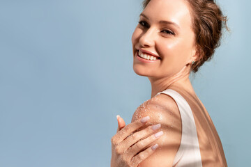 A beautiful tender woman put a natural cosmetic scrub to her shoulder and smiles - obrazy, fototapety, plakaty