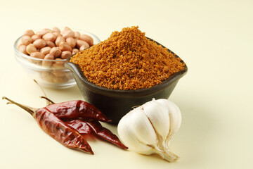 Powdered Garlic, coconut Chutney in a black bowl with garlic bulb, red chilies and groundnuts in a glass bowl, all places on a yellow background 