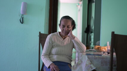 A hispanic older woman sitting alone at apartment. A pensive latin senior person