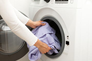 Woman loading dirty colored clothes into washing machine for washing in utility room