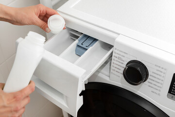 A woman pours gel powder into a washing machine close-up.