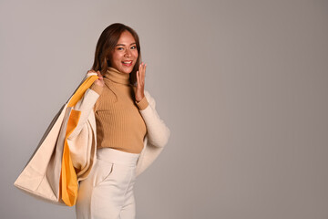 Beautiful young woman in warm clothes carrying tote bags standing isolated on grey background. Copy space for your text