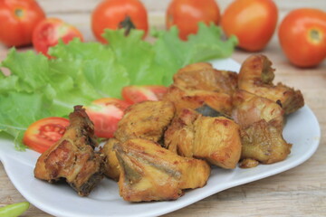 Fried chicken on a white plate with lettuce and tomato slices on a wooden table