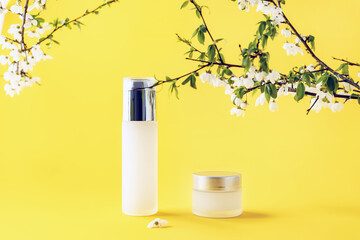 cosmetic containers and a sprig of plum blossoms on a yellow background, selective focus