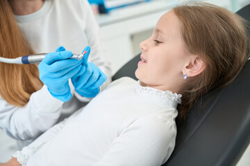 Fototapeta premium Pediatric dentist telling about teeth-polishing procedure to smiling little girl