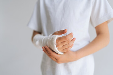 Close-up cropped shot of unrecognizable little girl with broken hand wrapped in white plaster...