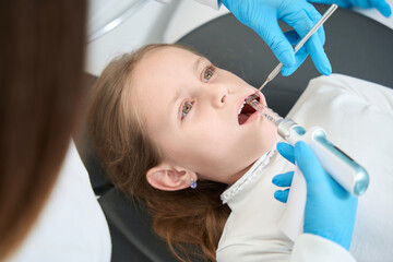 Fototapeta premium Pediatric dentist administering local anesthesia to little girl